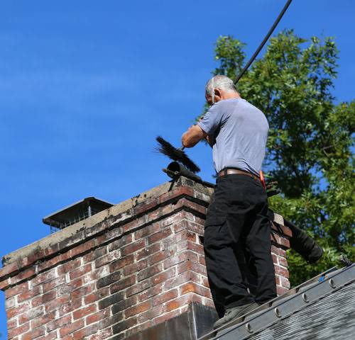 Technician servicing exterior chimney components above the roofline