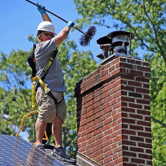 Roof technician brushing a residential chimney near its cap